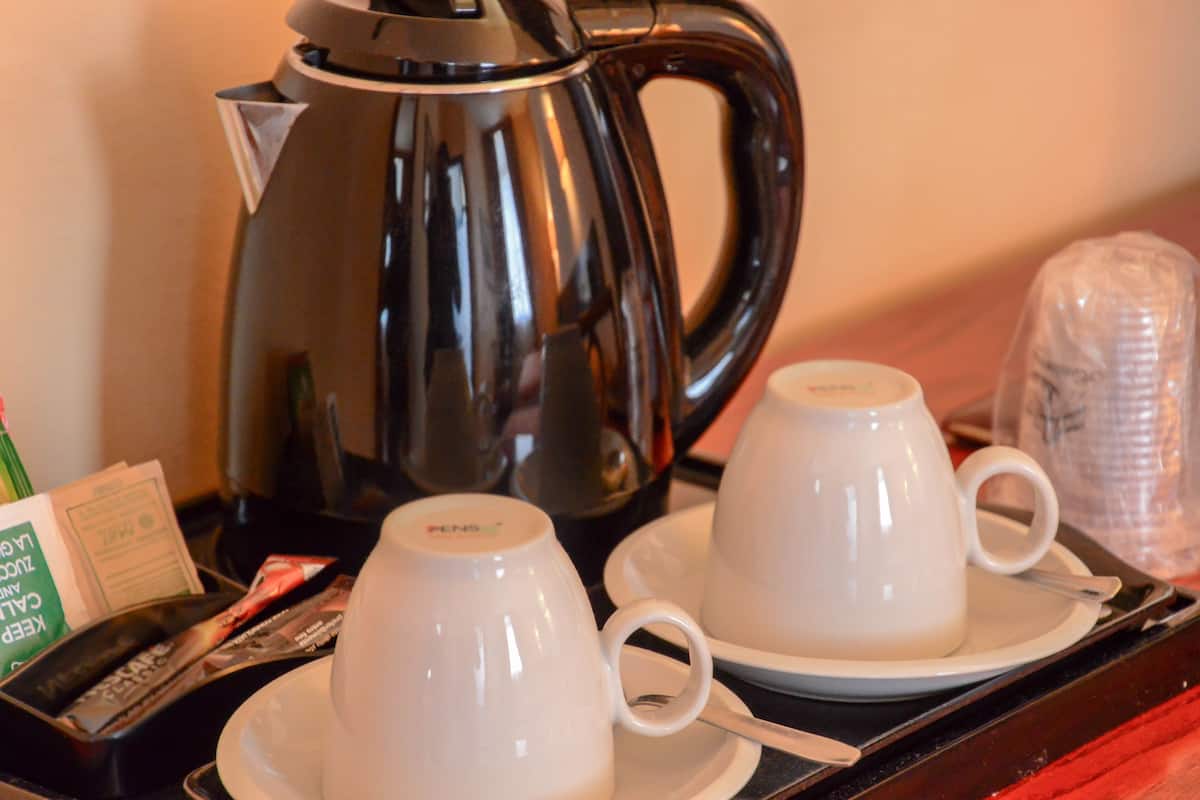 A tray with a black coffee pot, two white cups, and a plastic container.
