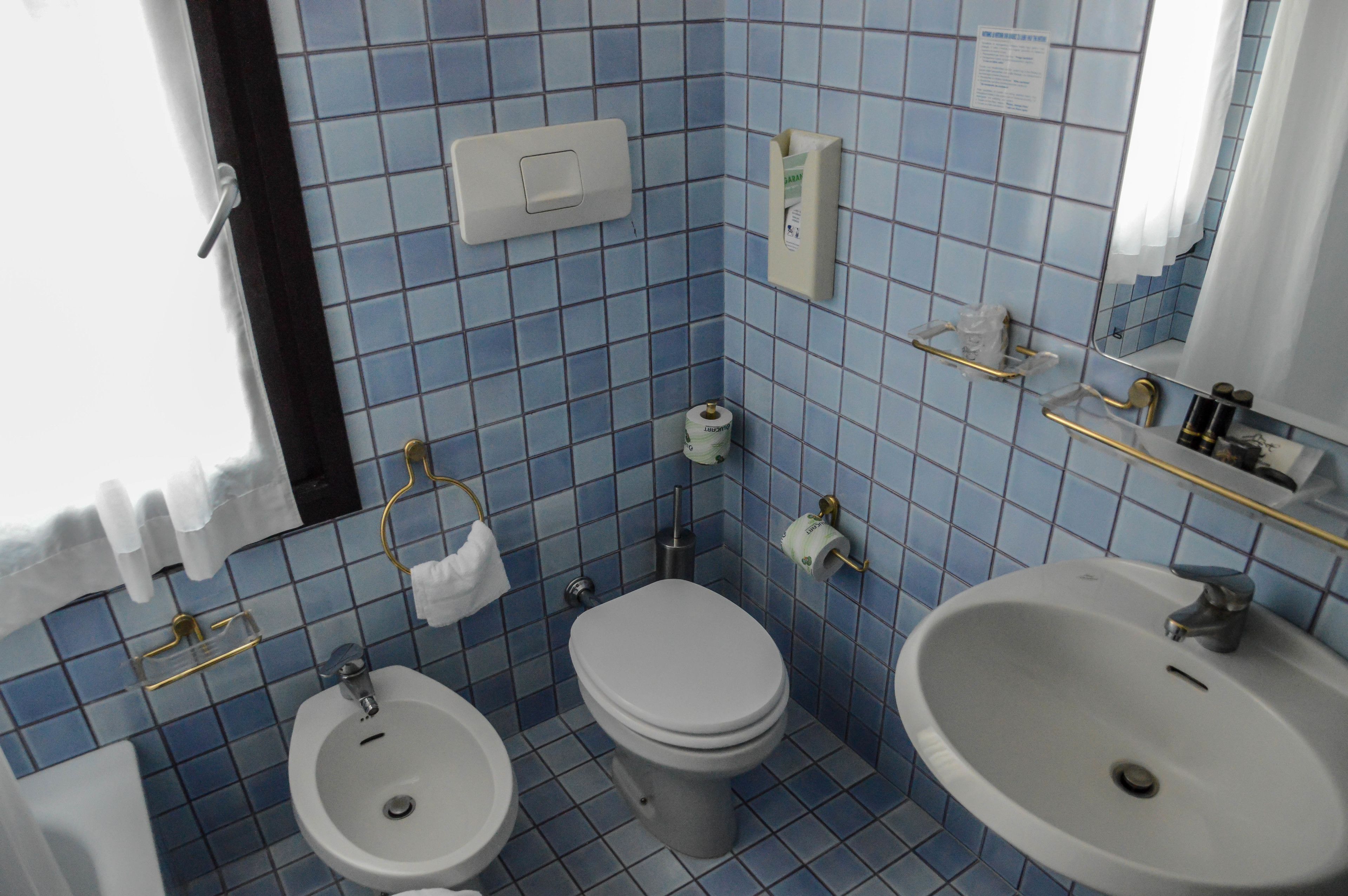 A bathroom with a toilet, bidet, and sink, tiled in blue.