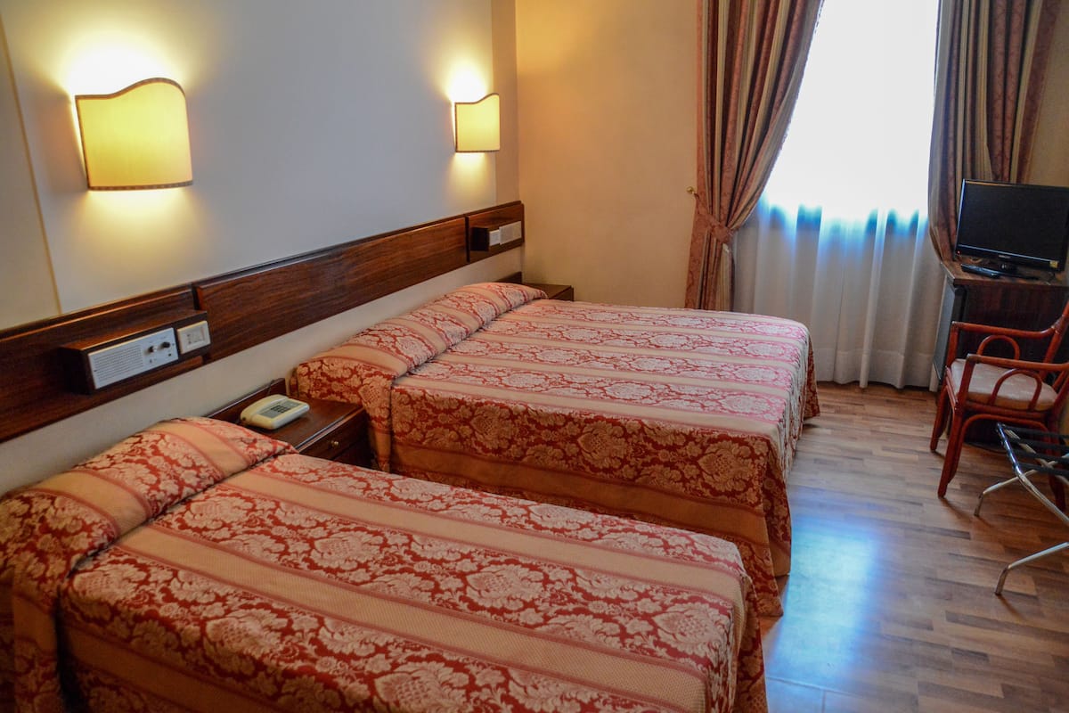 A hotel room with two beds, a desk with a television, and a chair.