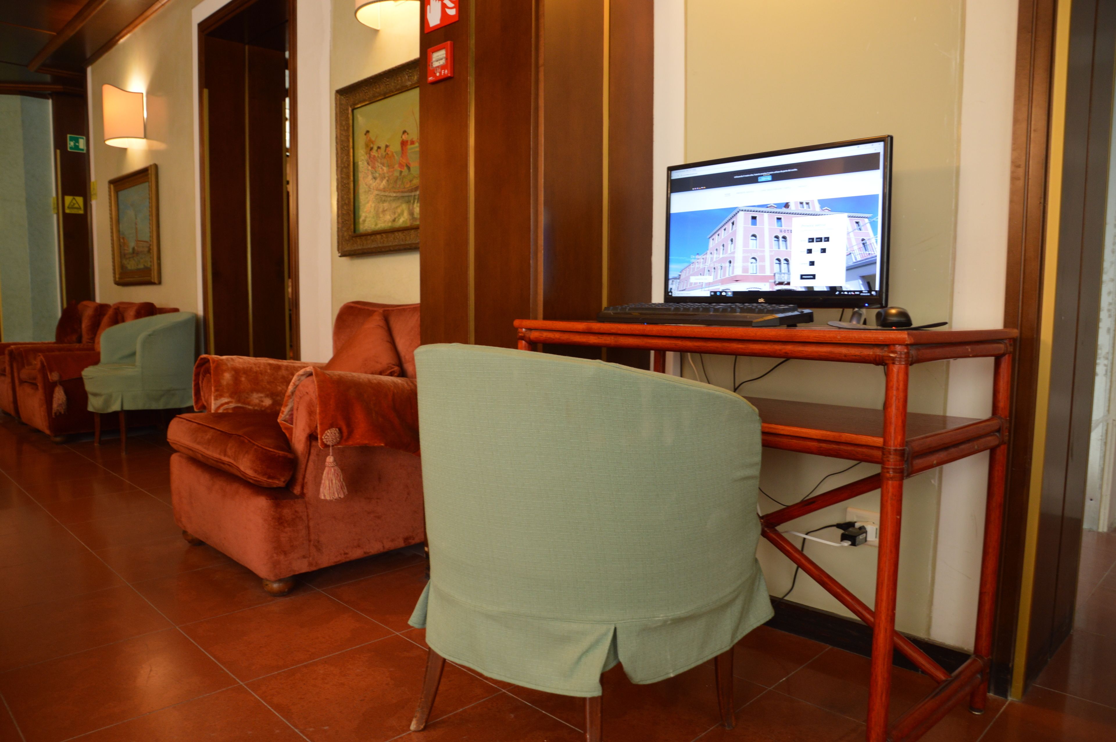 A hotel lobby with a seating area featuring a sofa and chairs, a wooden desk with a laptop, and a framed picture on the wall.