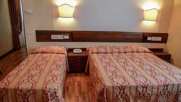 A hotel room with two beds, wooden headboards, bedside tables, and wall-mounted lamps.