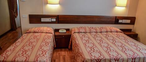 A hotel room with two beds, wooden headboards, bedside tables, and wall-mounted lamps.