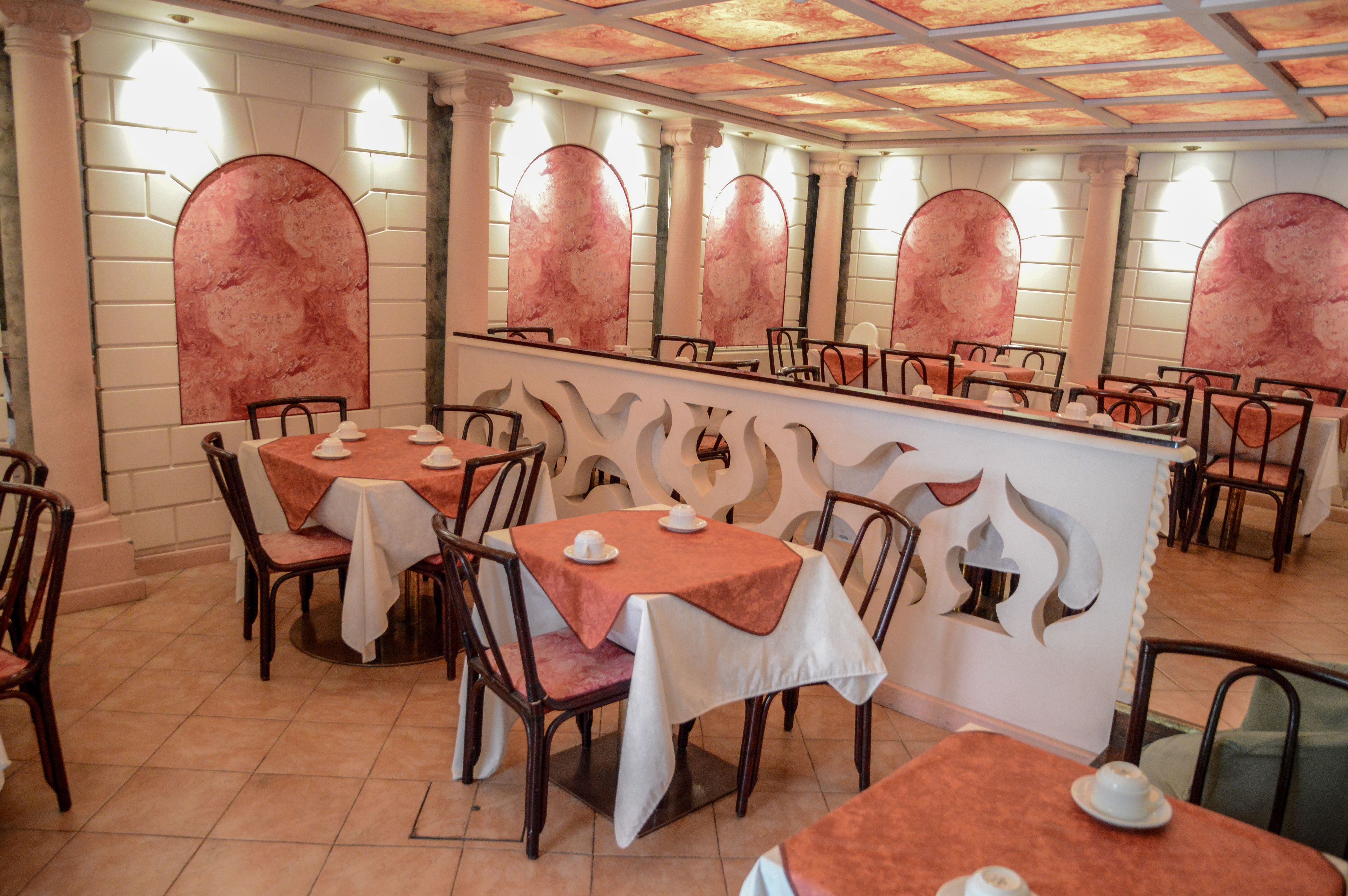 A restaurant with multiple tables and chairs, each with a white tablecloth and a teapot.