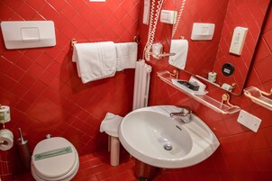 A bathroom with a red tiled wall, white sink, and a toilet with a green sign.