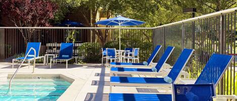 A poolside area with blue lounge chairs and umbrellas, a pool, and a table with drinks.