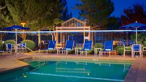 A pool area with lounge chairs and umbrellas, surrounded by trees and a building with a triangular roof. - Sonesta ES Suites Flagstaff (Flagstaff)