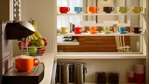 A kitchen with a coffee machine, a fruit bowl, and a shelf with colorful cups and saucers. - Sonesta ES Suites Flagstaff (Flagstaff)