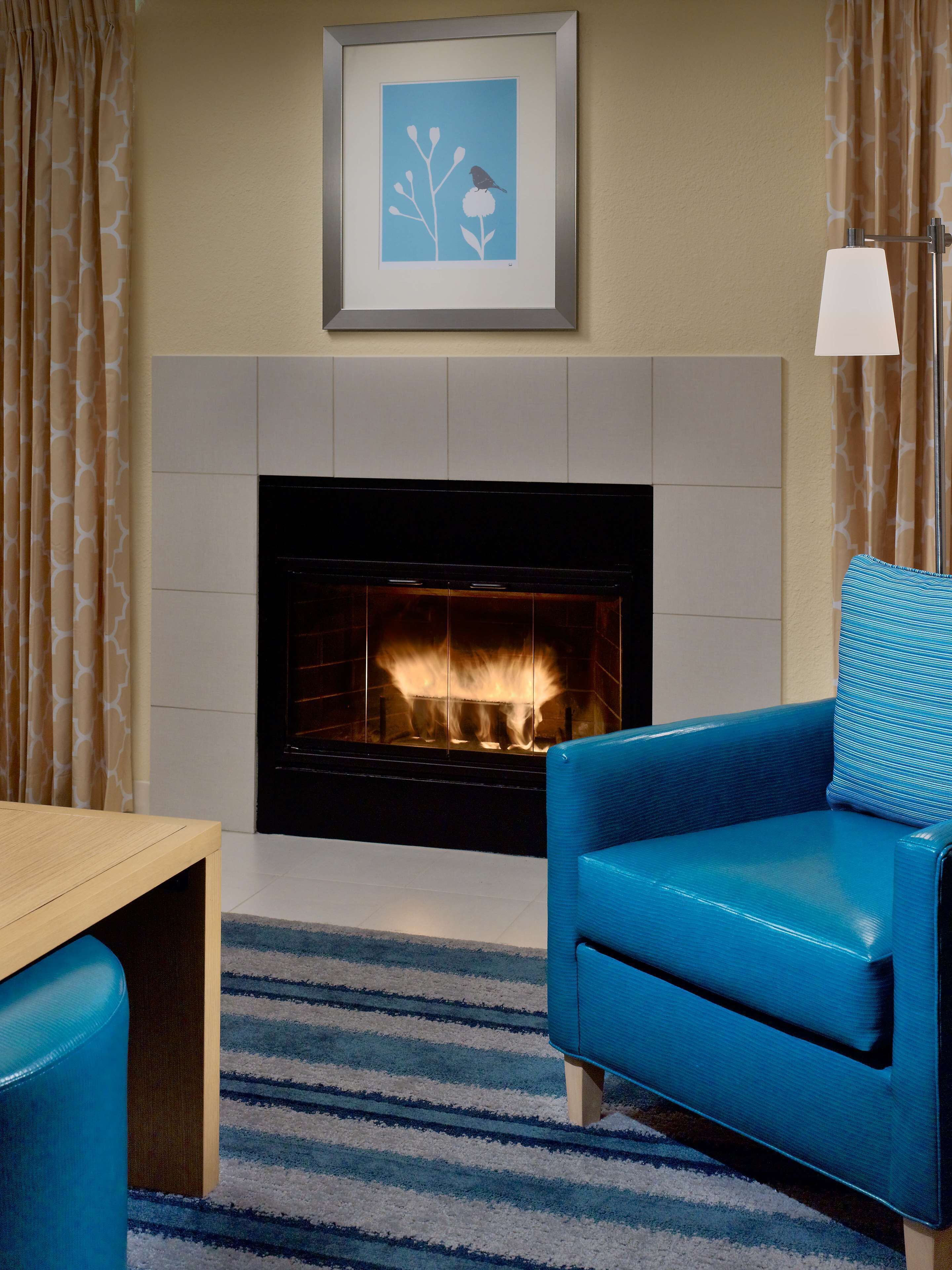 Una sala de estar con chimenea, un cuadro colgado encima y un sillón azul.
