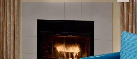Una sala de estar con chimenea, un cuadro colgado encima y un sillón azul.