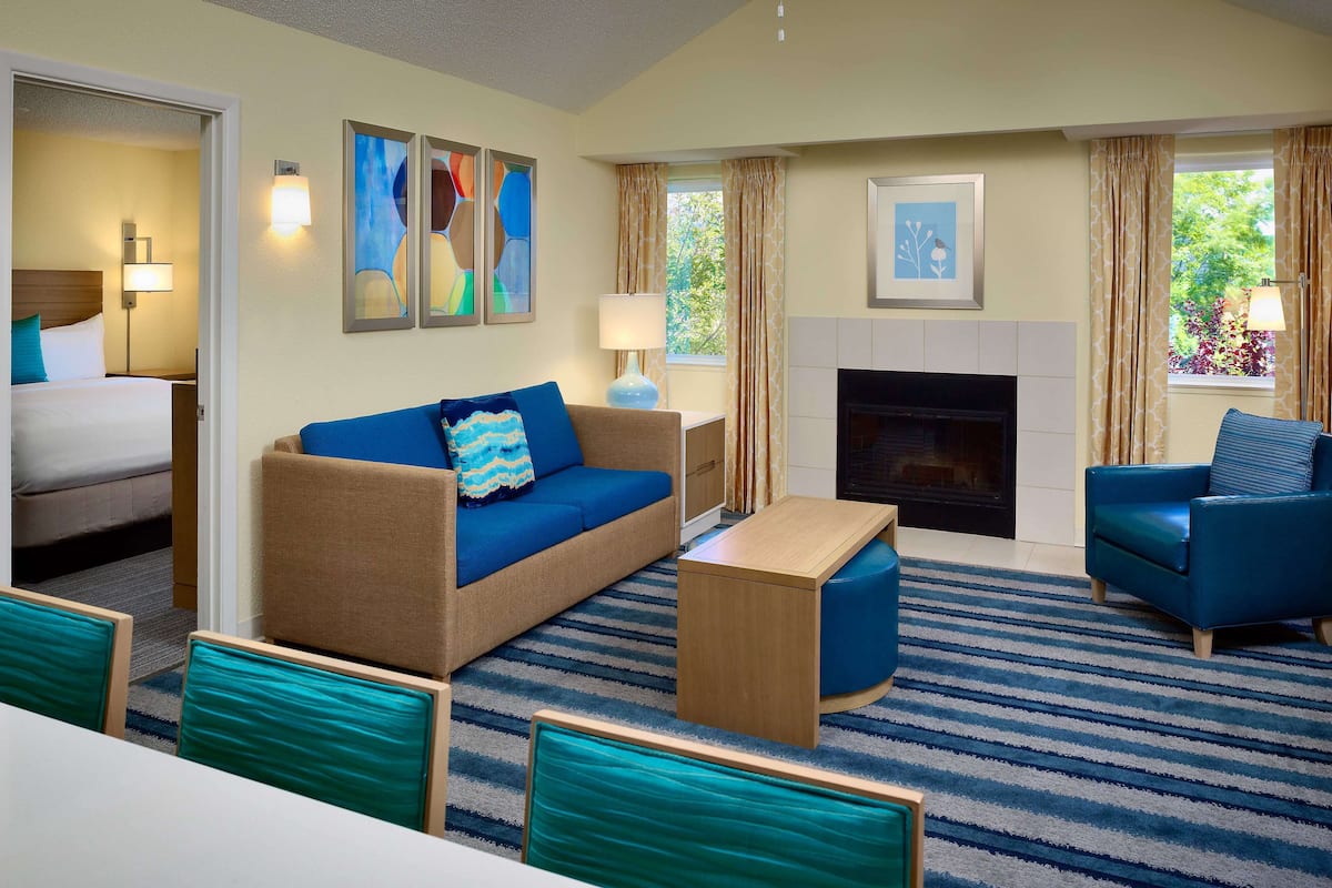 Une chambre d’hôtel avec un lit, un canapé bleu, un fauteuil bleu, une table basse en bois et une cheminée.