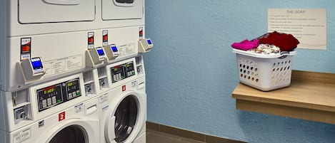A laundry room with stacked washers and dryers, a payment terminal, and a basket of laundry on a shelf.