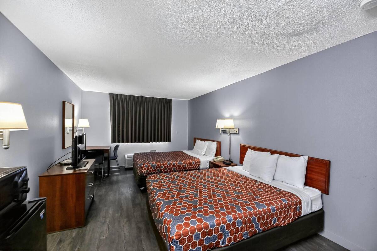 A hotel room with two beds, a desk, a TV, and a window with curtains.