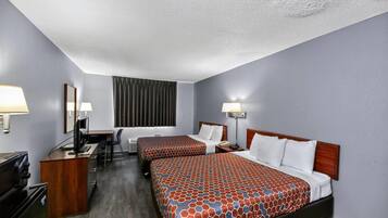 A hotel room with two beds, a desk, a TV, and a window with curtains.