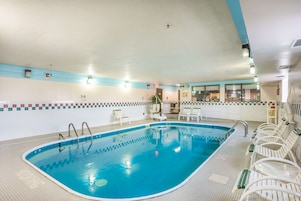 Una piscina interior con carriles delimitados, suelo de baldosas y sillones blancos a lo largo del borde.