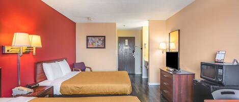 A hotel room with two beds, a desk with a microwave, a TV, and a dresser.