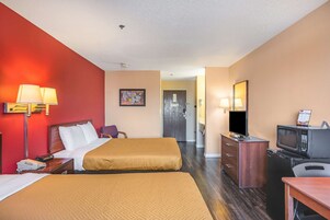 A hotel room with two beds, a desk with a microwave, a TV, and a dresser.