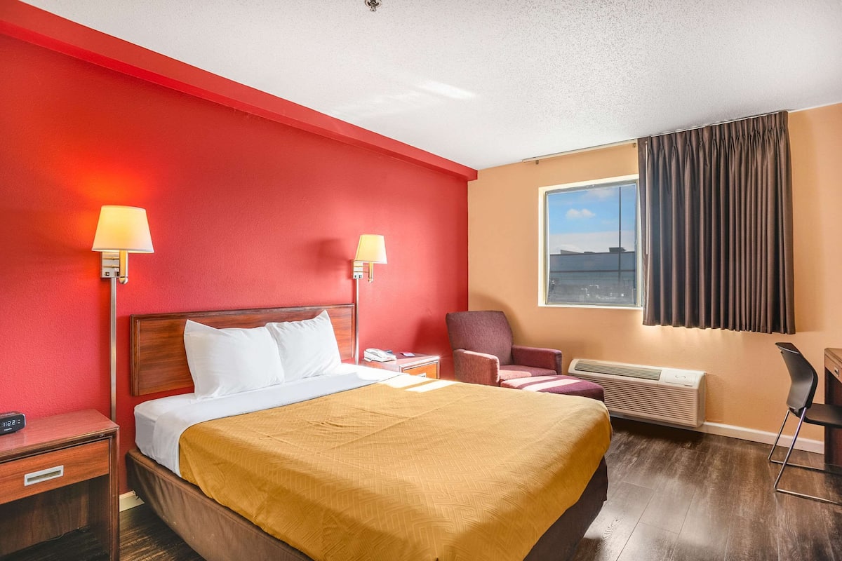 A hotel room with a large bed, two bedside lamps, a chair, a desk, and a window with curtains.
