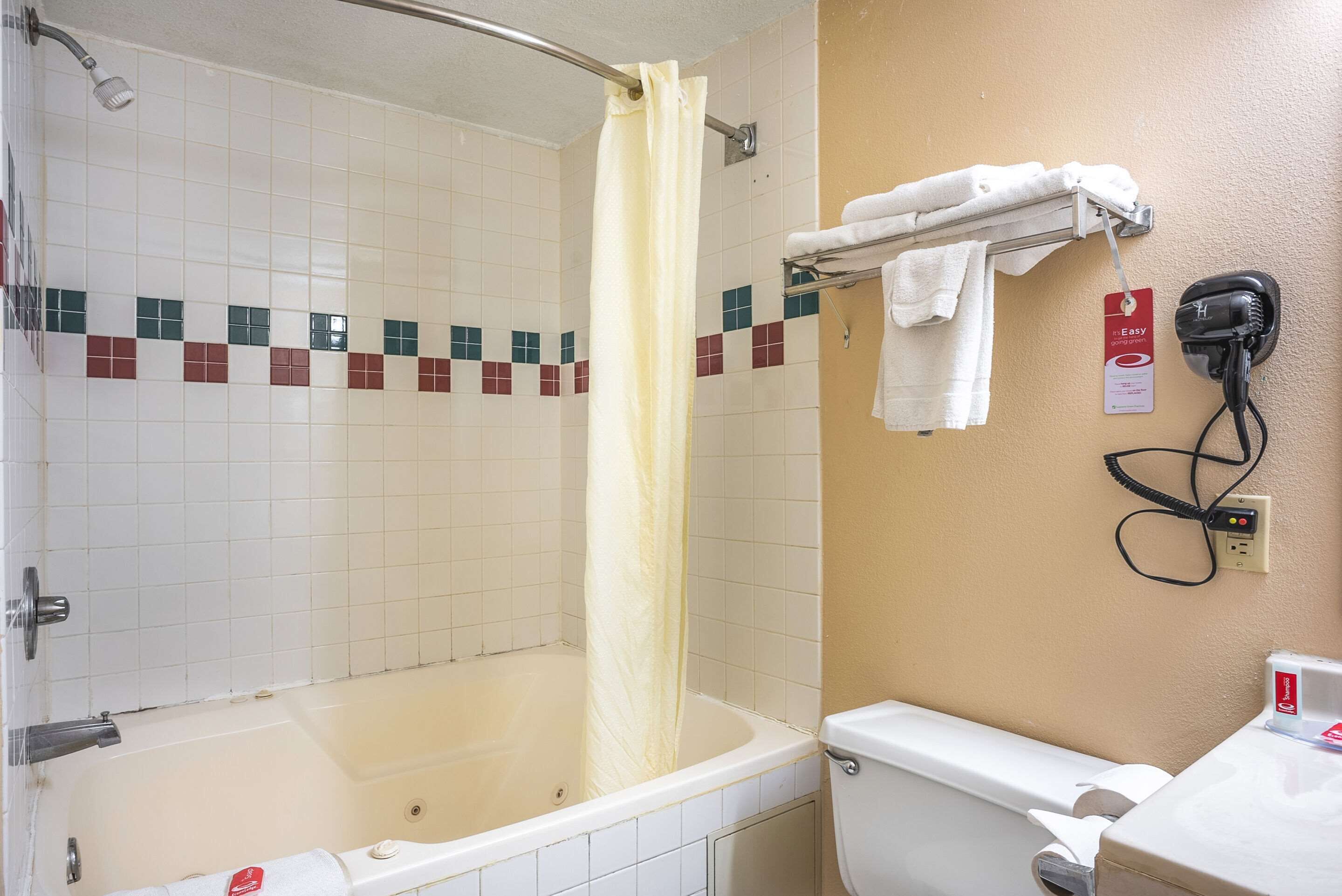 Een badkamer met een bad, douchegordijn, handdoekrek en een föhn aan de muur.