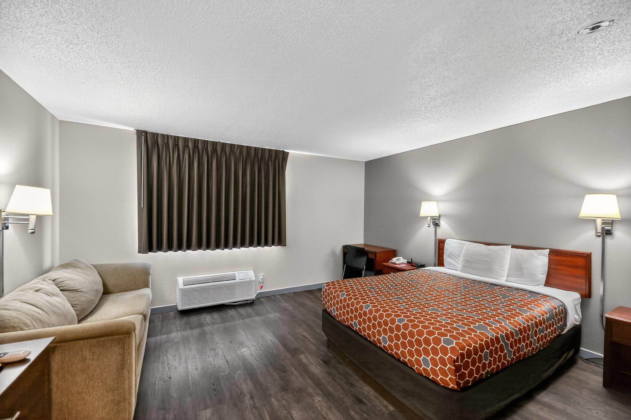 A hotel room with a bed, a sofa, a desk, a lamp, and a window with curtains.
