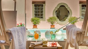 A poolside lounge with two sun loungers, a table with drinks and snacks, and potted plants.