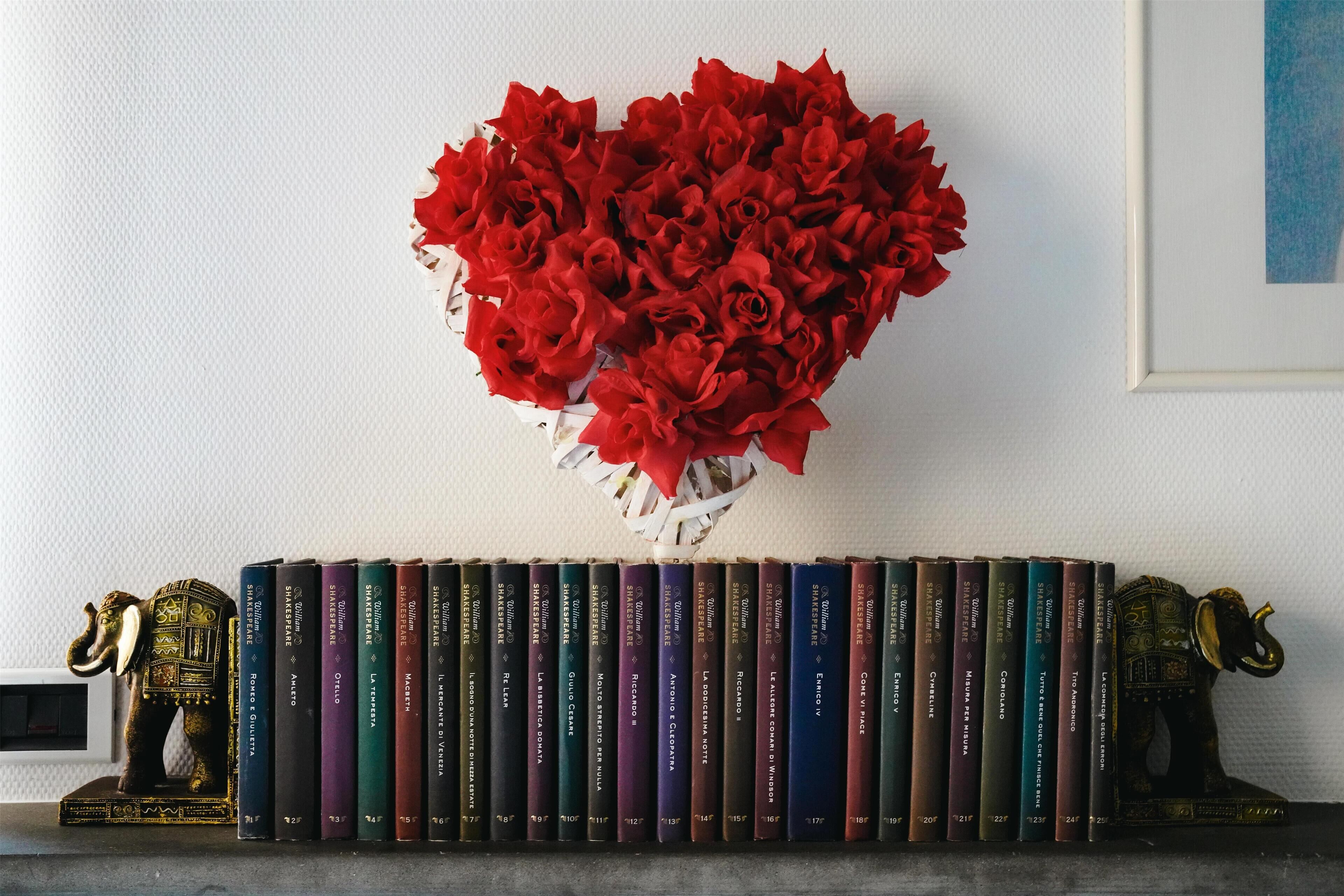 Une bibliothèque sur laquelle est posé un bouquet de roses rouges en forme de cœur, entouré de livres et de deux statuettes d’éléphants.
