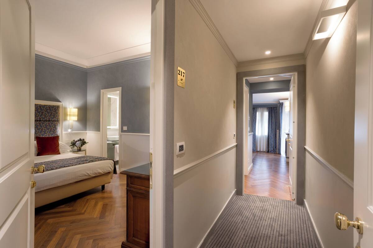 Une chambre d’hôtel avec un lit, une table de chevet, une lampe et une porte donnant sur une autre pièce.