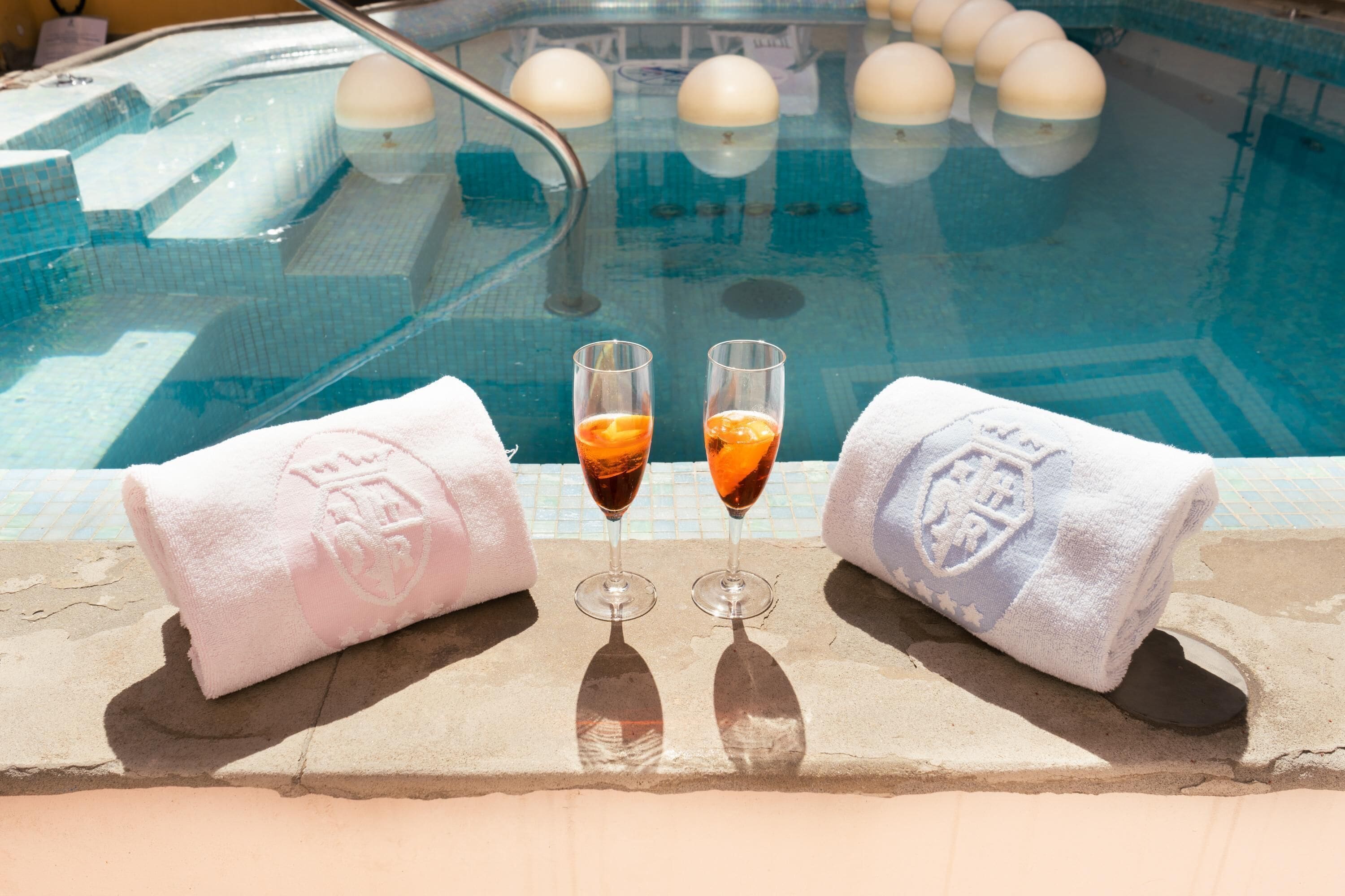 A poolside area with two towels and two glasses of a dark beverage.