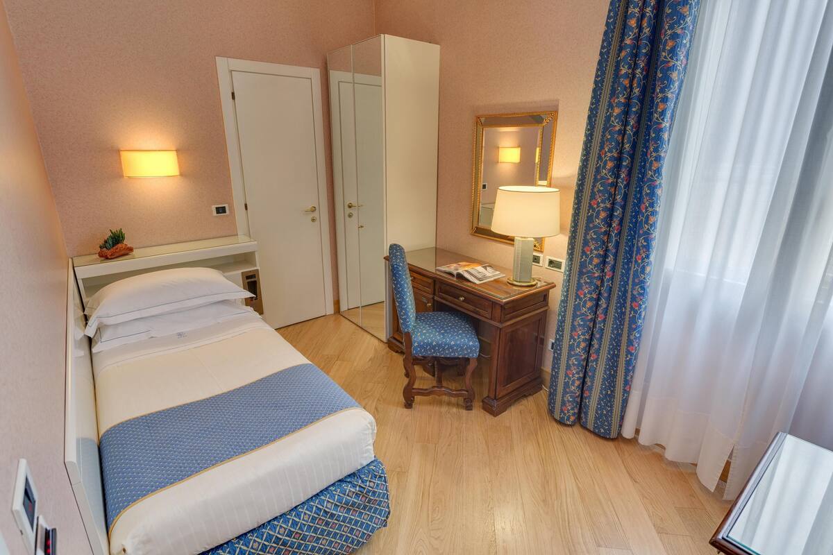 Une chambre d’hôtel comprenant un lit, un bureau, une chaise, une armoire et un miroir.