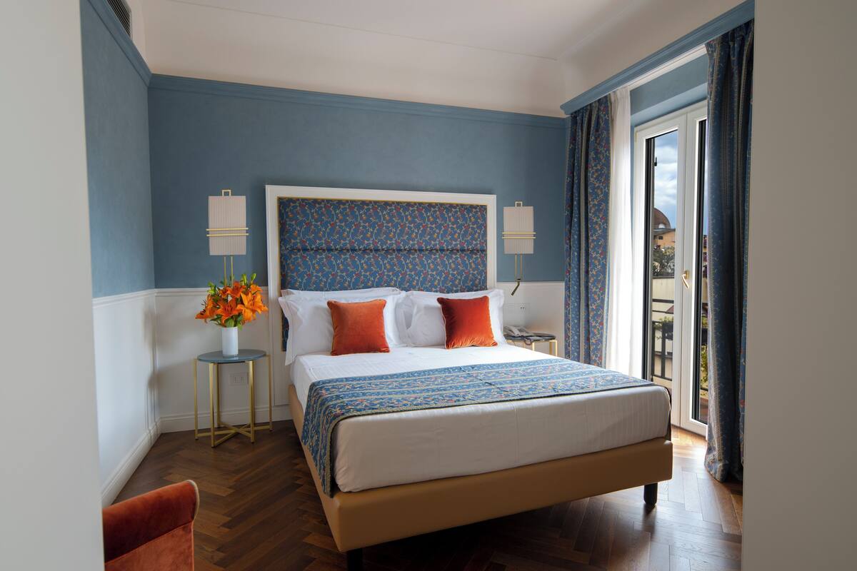 Une chambre avec un grand lit, deux tables de chevet, une commode, une chaise et une vue sur l’extérieur.