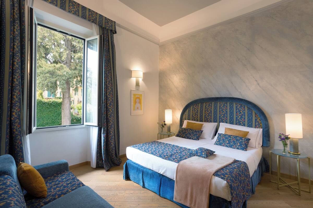 Une chambre à coucher avec un grand lit, un canapé, une fenêtre avec des rideaux et une lampe sur une table de chevet.