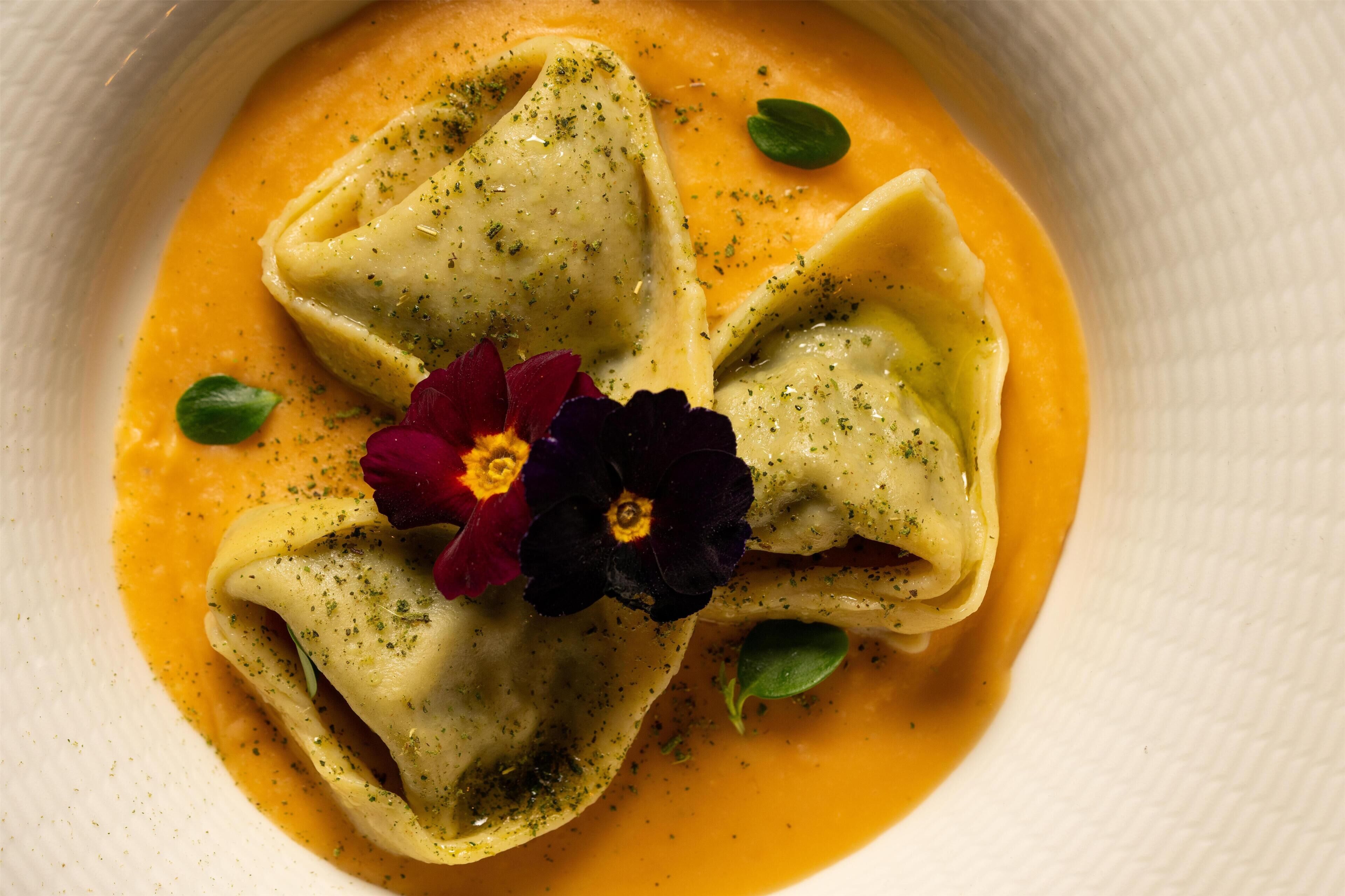Un plat de raviolis nappés d’une sauce crémeuse, décoré d’herbes et de fleurs.