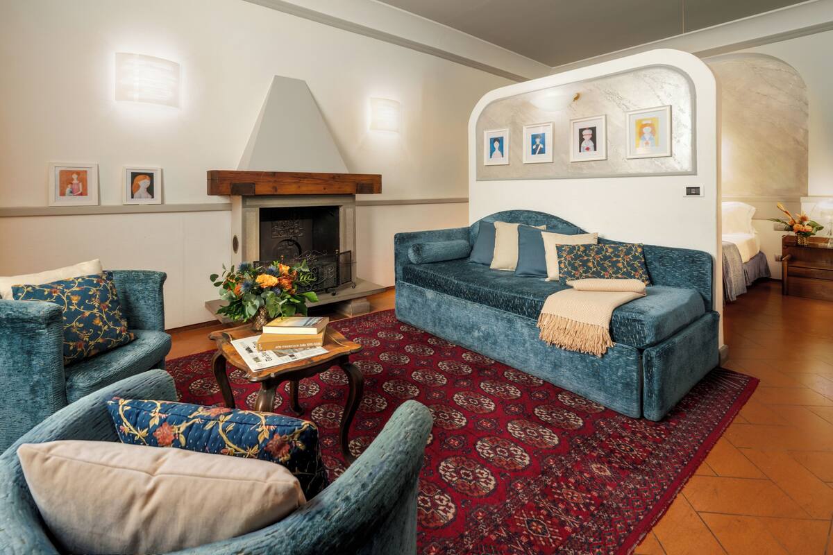 Un salon avec un canapé, des fauteuils, une cheminée et un tapis rouge à motifs.