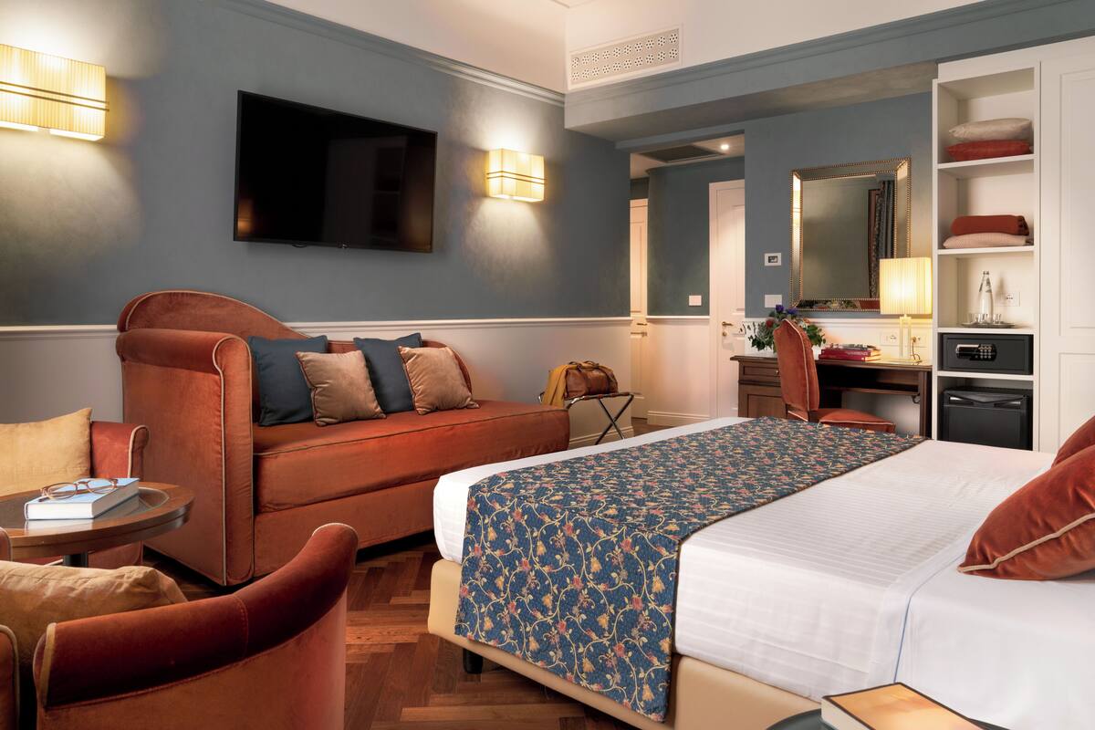 Une chambre d’hôtel avec un lit, un canapé, un bureau, une télévision et un miroir.