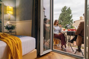 A hotel room with a bed, a glass door leading to an outdoor seating area, a lamp, and a vase with flowers.