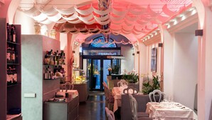 A restaurant interior with a central archway, tables set for dining, and shelves with bottles.