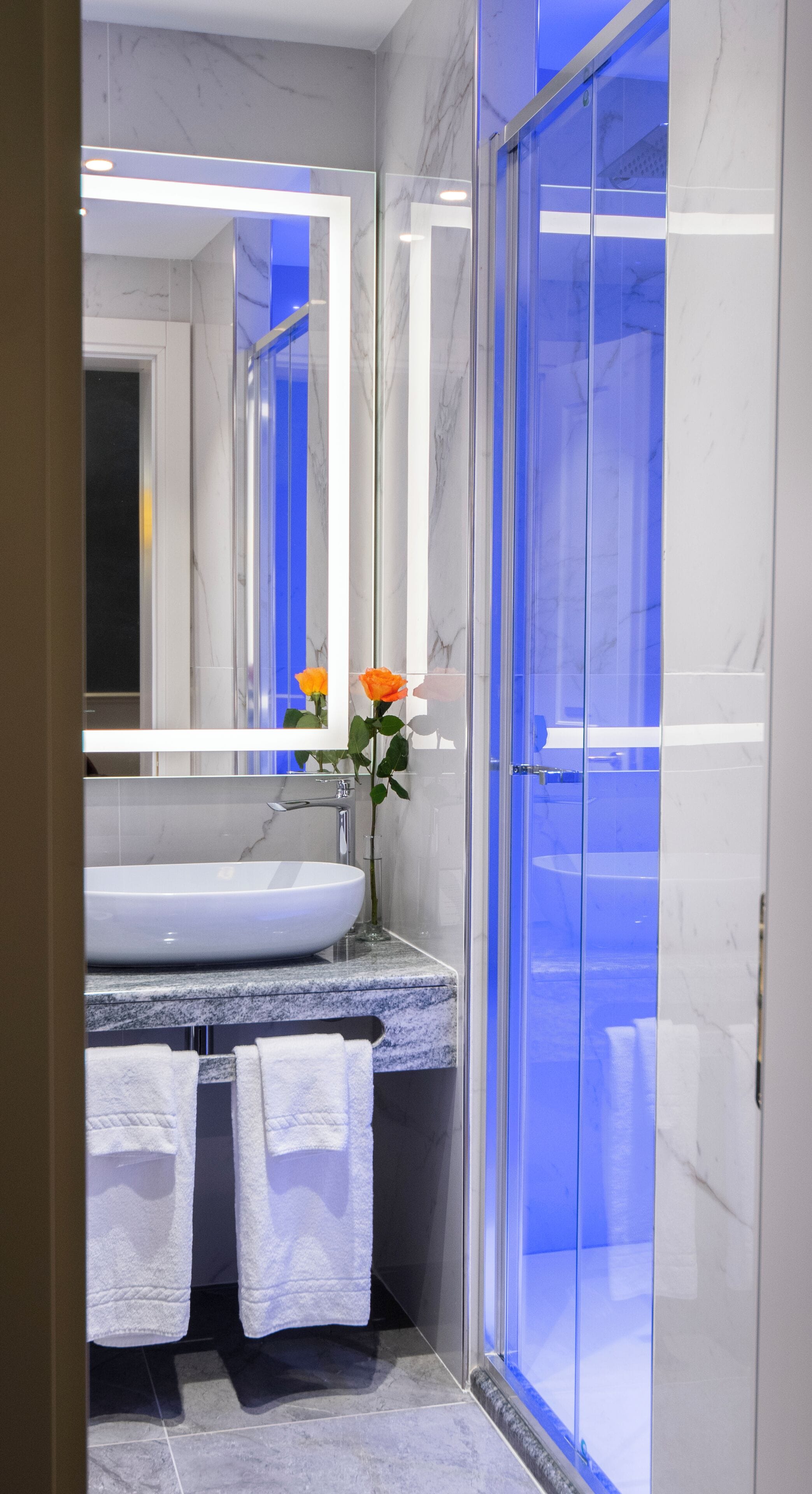 A modern bathroom with a large mirror, a white sink, and a glass shower enclosure.