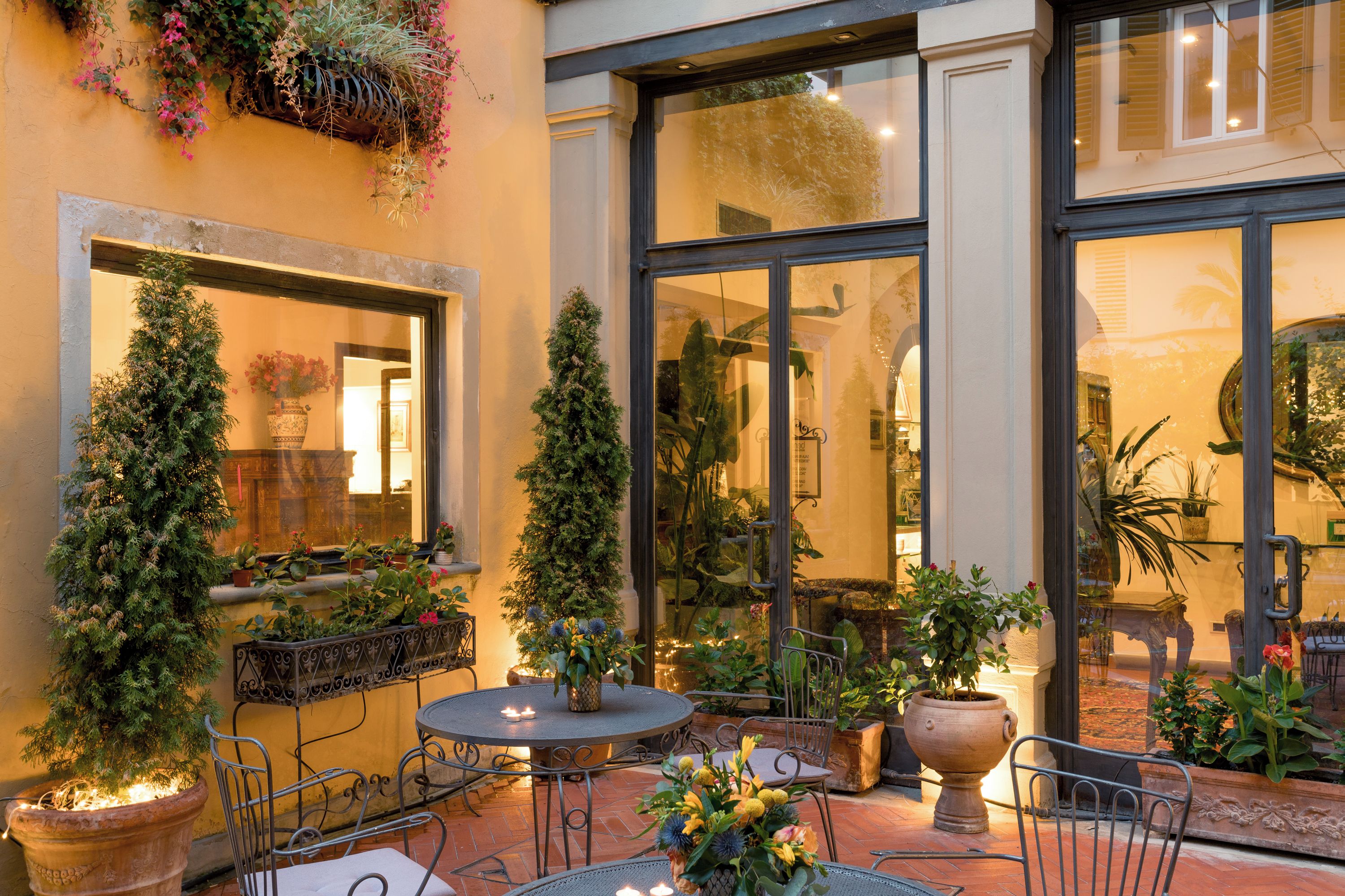 Eine Terrasse im Freien mit einem runden Tisch, Stühlen, Blumentöpfen und einem großen Fenster.