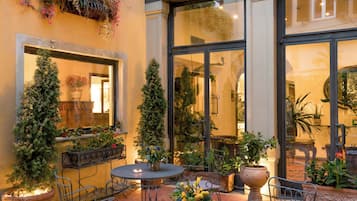 Eine Terrasse im Freien mit einem runden Tisch, Stühlen, Blumentöpfen und einem großen Fenster.