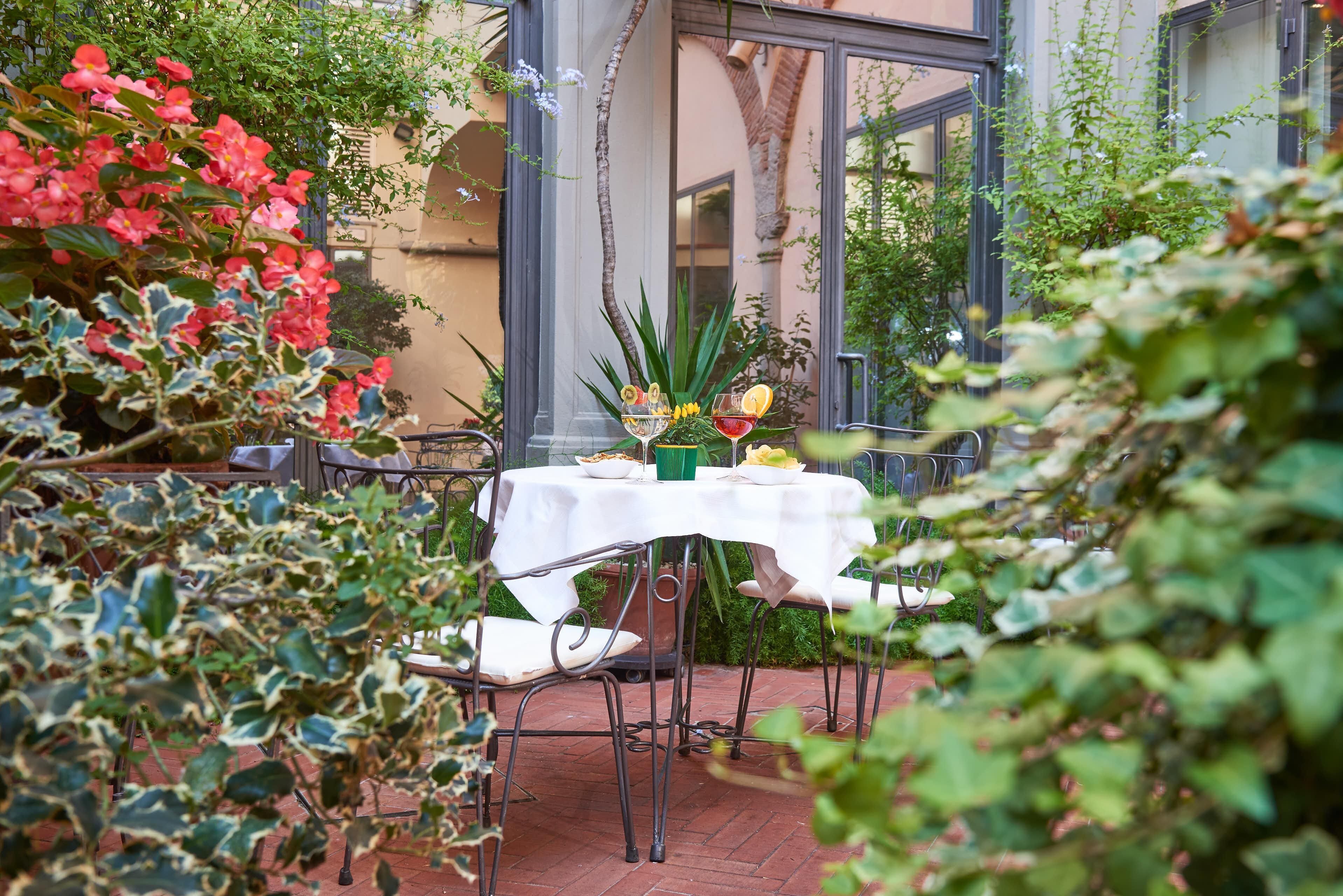Un espace de restauration en plein air avec une table dressée pour deux personnes, entouré d’une végétation luxuriante et doté d’un sol en briques.