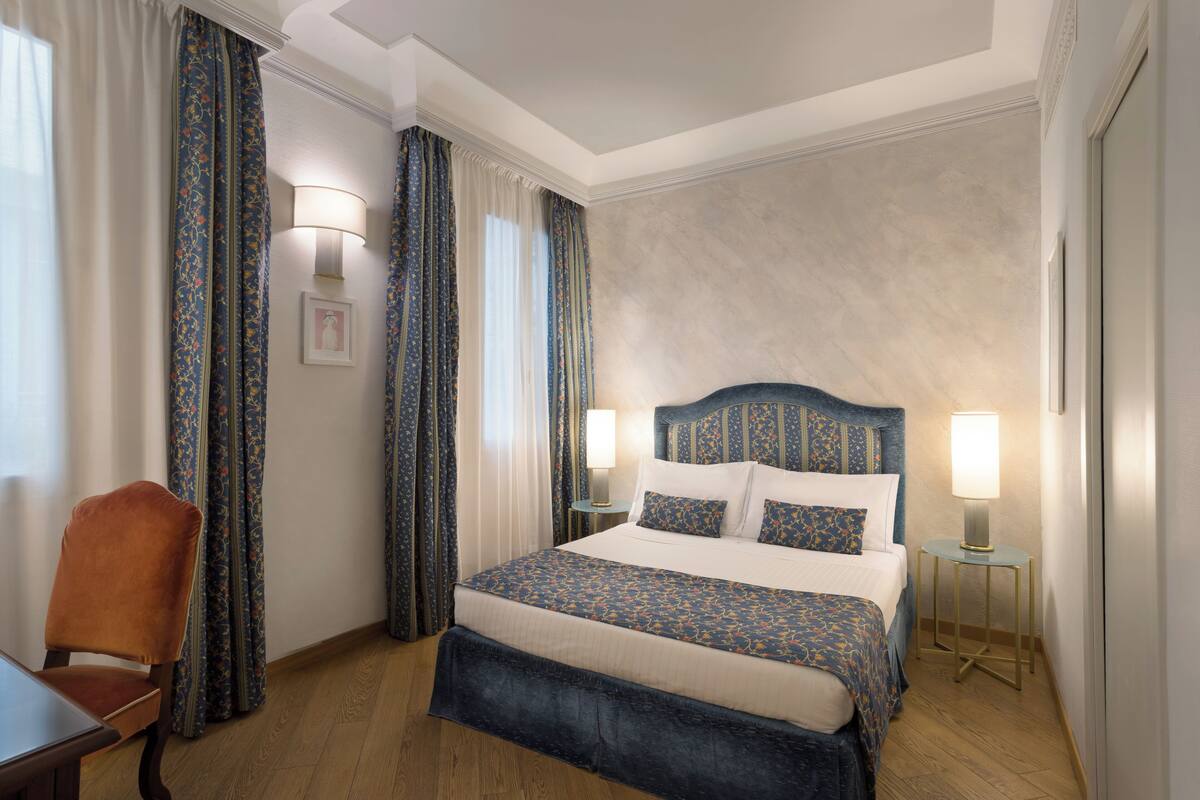 Une chambre d’hôtel avec un lit, une chaise, une table de chevet et une lampe.
