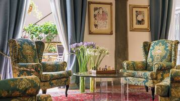 Een kamer met twee fauteuils, een schaakbord, een vaas met bloemen en twee ingelijste kunstwerken aan de muur.