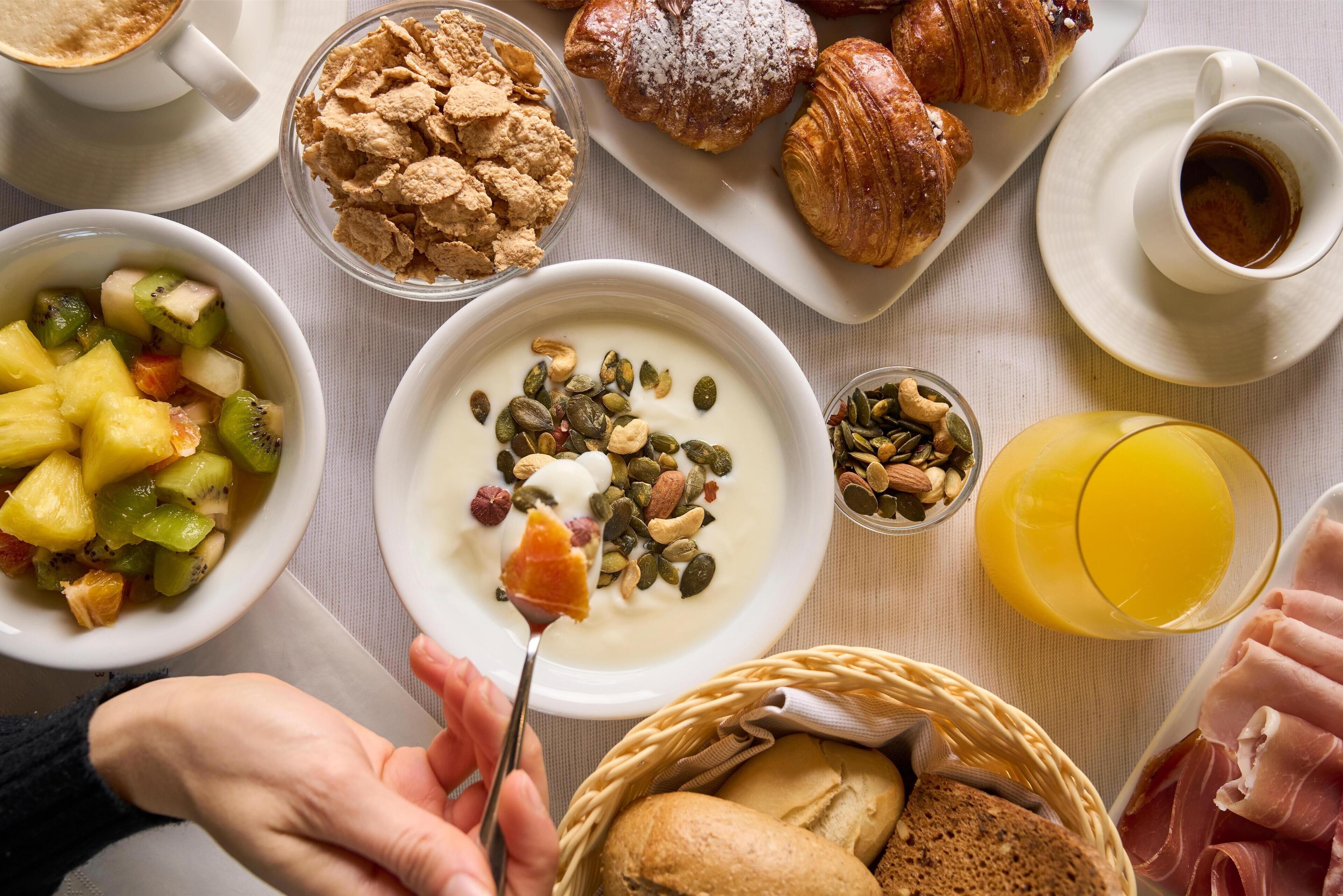 Et morgenmåltid med forskellige spisemuligheder, herunder croissanter, müsli, frugt, yoghurt og kager.