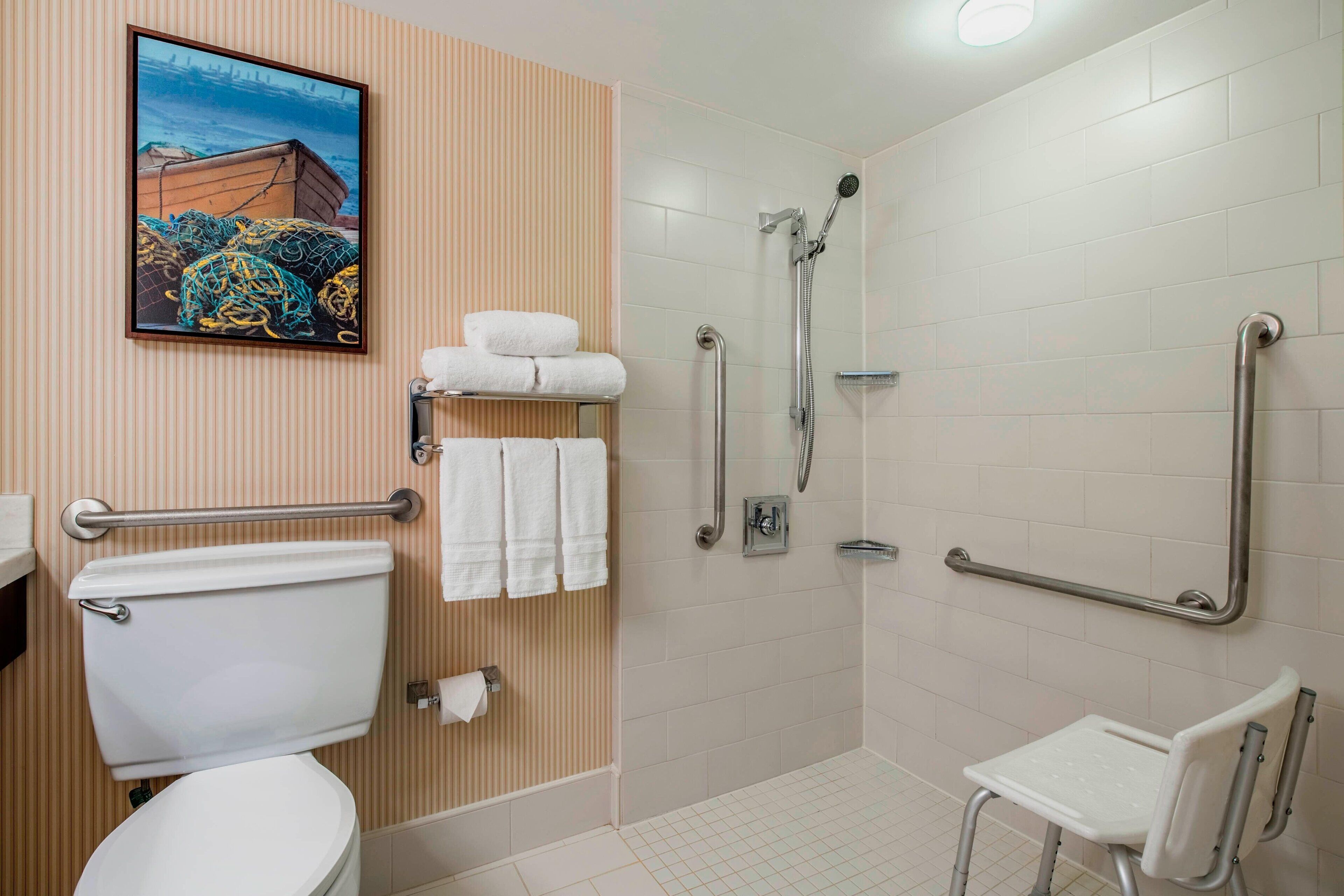 A bathroom with a toilet, a shower with grab bars, a wheelchair-accessible bench, and a towel rack.