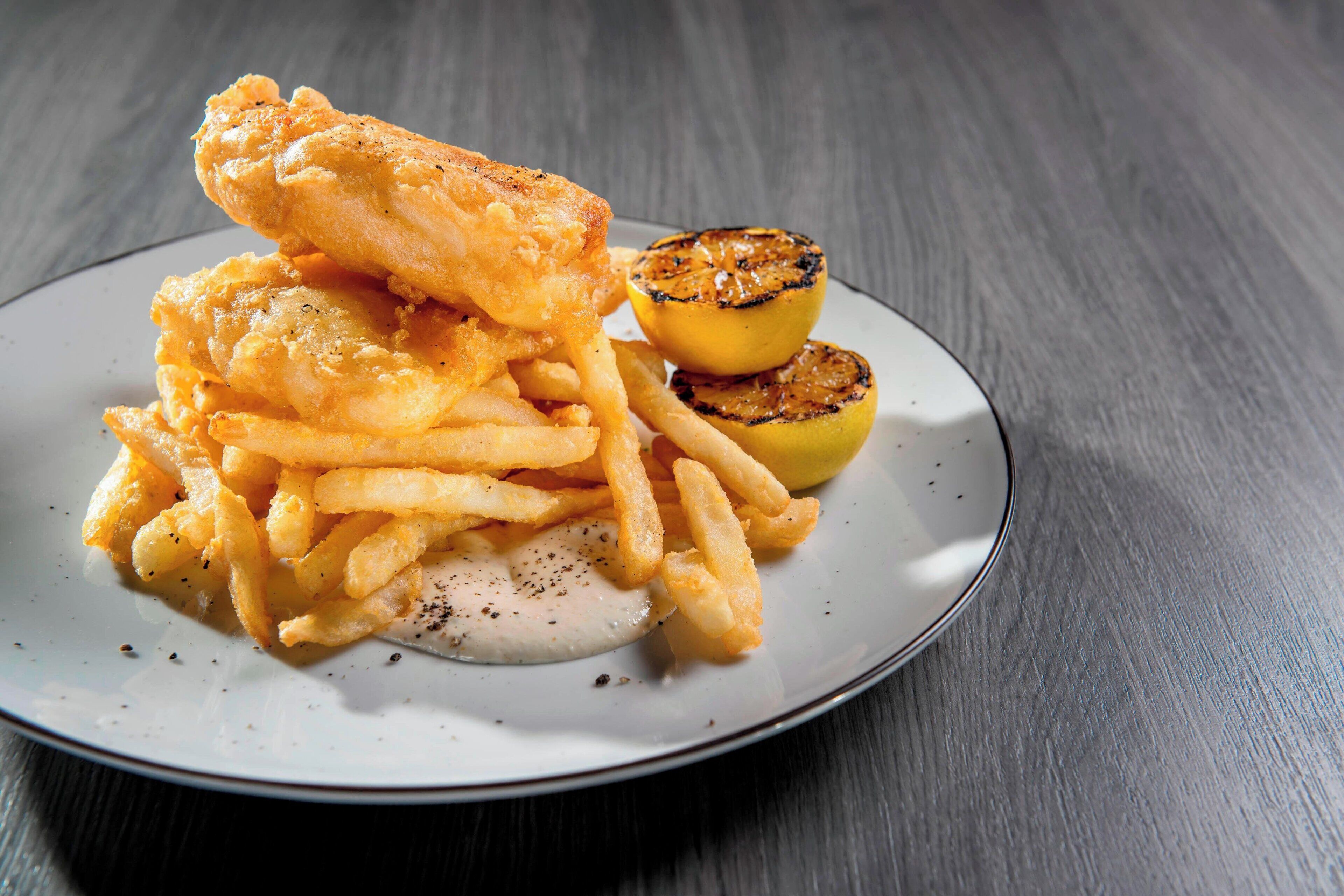 A plate of fish and chips with lemon wedges.