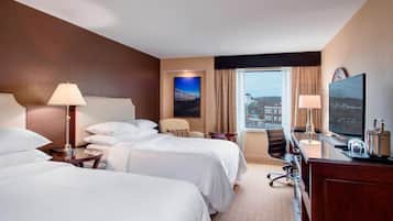 A hotel room with two beds, a desk with a television, a chair, and a window with a city view.