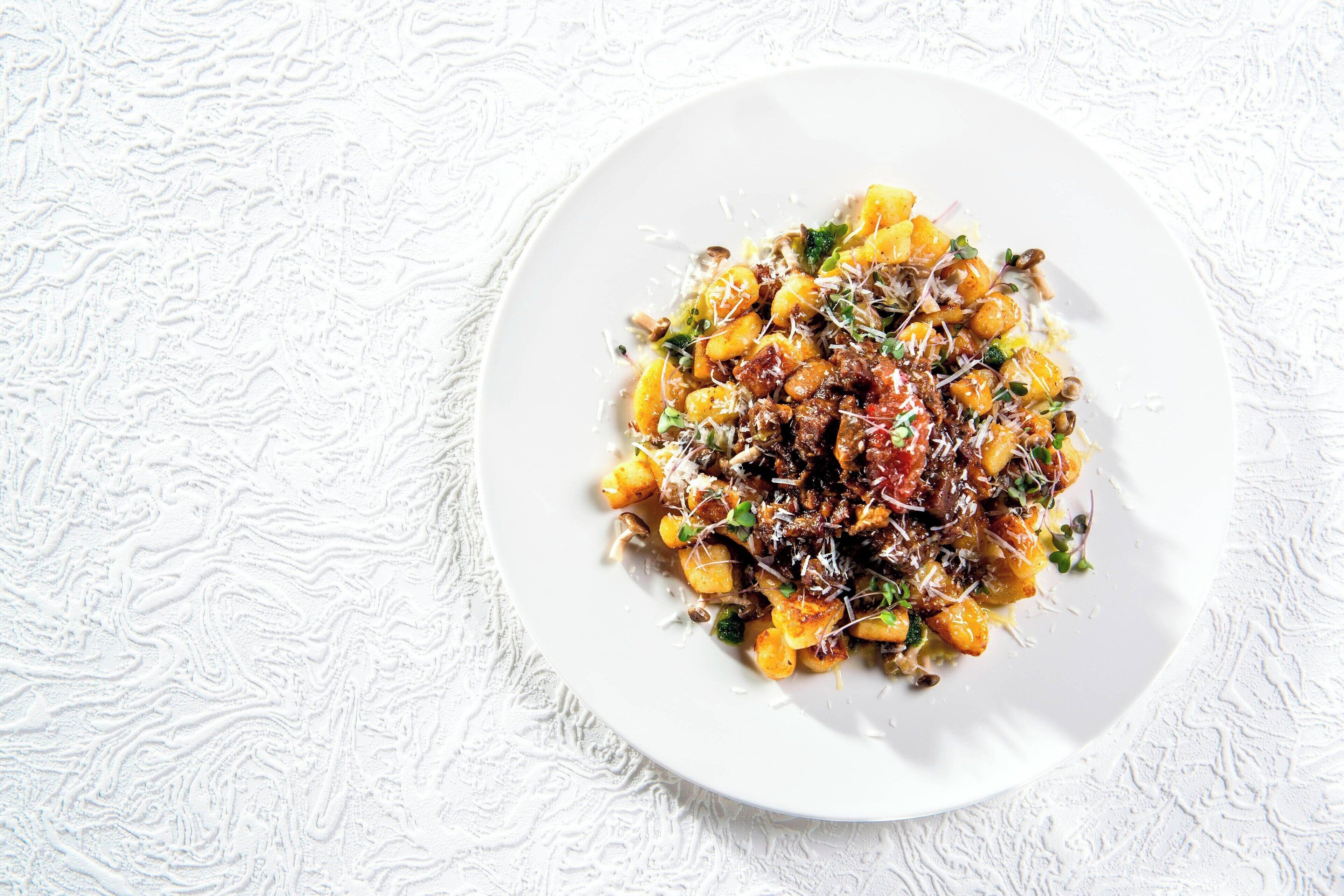 A white plate with a pasta dish on a textured white surface.