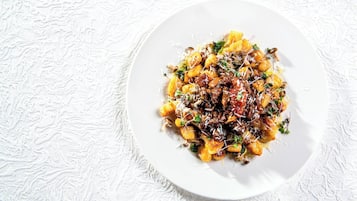A white plate with a pasta dish on a textured white surface.