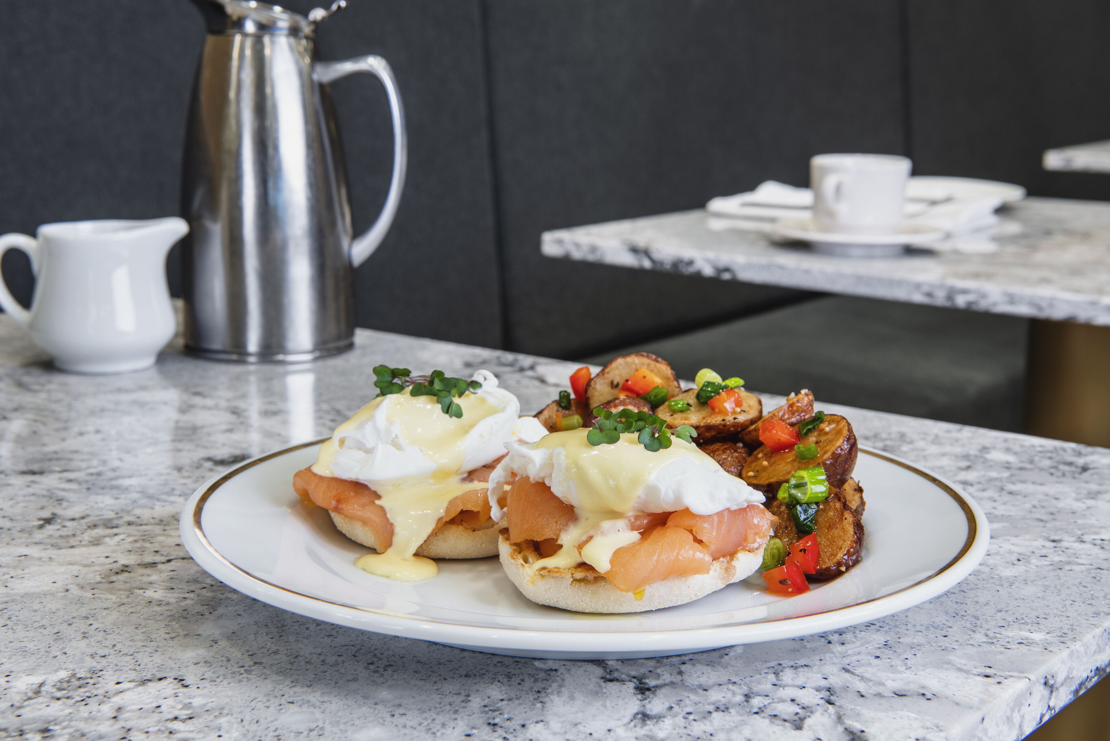 A breakfast plate with eggs benedict and toast, a white pitcher, and a cup on a marble table.