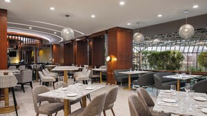 Un restaurante moderno con mesas de mármol y sillas tapizadas, que presenta un muro de madera curvada y lámparas esféricas colgantes.