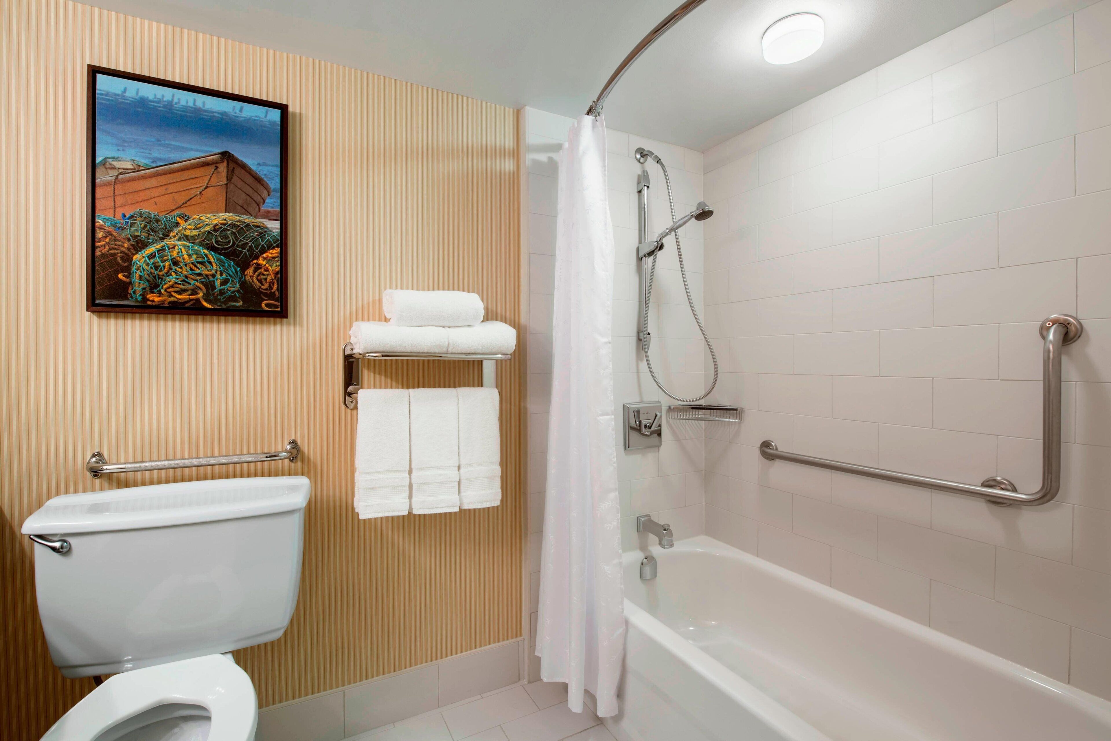Une salle de bain équipée de toilettes, d’une douche avec des barres d’appui et d’un porte-serviettes.